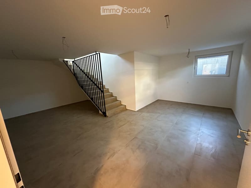Empty room with tiled floor, white walls, and a staircase leading upwards. Natural light enters through a window on the right side.