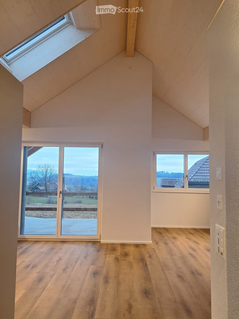 Bright, empty room with wooden flooring, large windows, and a sliding glass door leading to a scenic outdoor view.