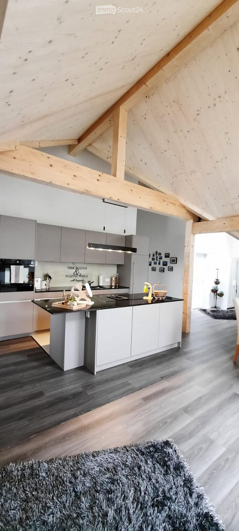 Modern kitchen with grey cabinetry, a central island, induction cooktop, and a sleek black countertop. Exposed wooden beams and dark hardwood flooring add warmth to the space.