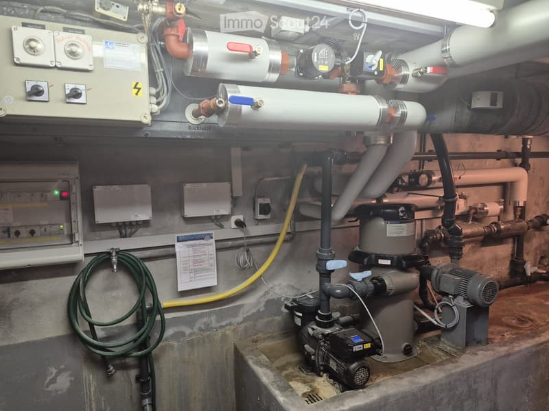 A utility room with various plumbing and heating equipment, including pipes, valves, a pump, and control panels.