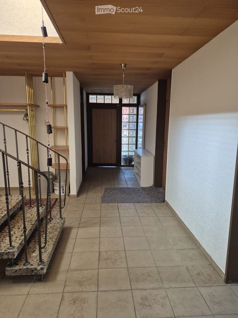 Hallway with tiled floor, staircase with metal railing, pendant light, small bench, and decorative wall shelves.