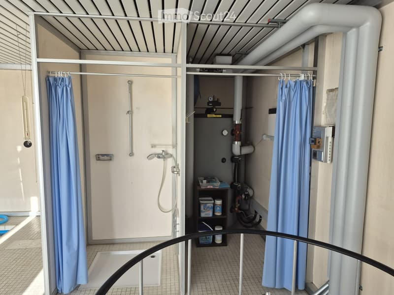 Compact bathroom with a shower stall, tiled floor, and storage shelf holding bins and cleaning supplies.