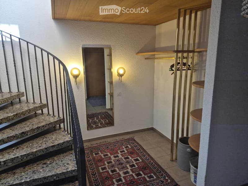 Staircase with patterned tiles, metal railing, and wall-mounted lamps. A small rug is placed on the floor, and a closet with a mirrored door is visible in the background.