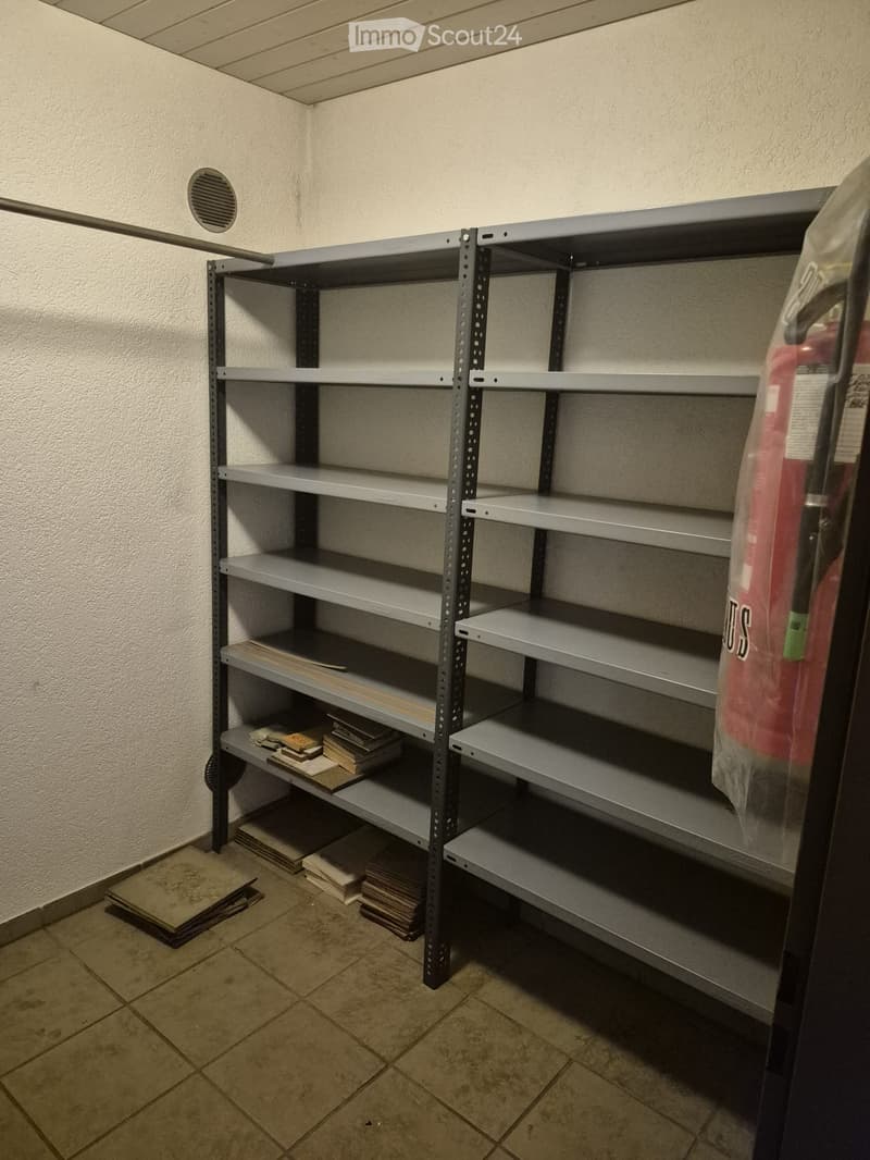 Empty storage room with metal shelving units, tiled floor, and a fire extinguisher on the right side.