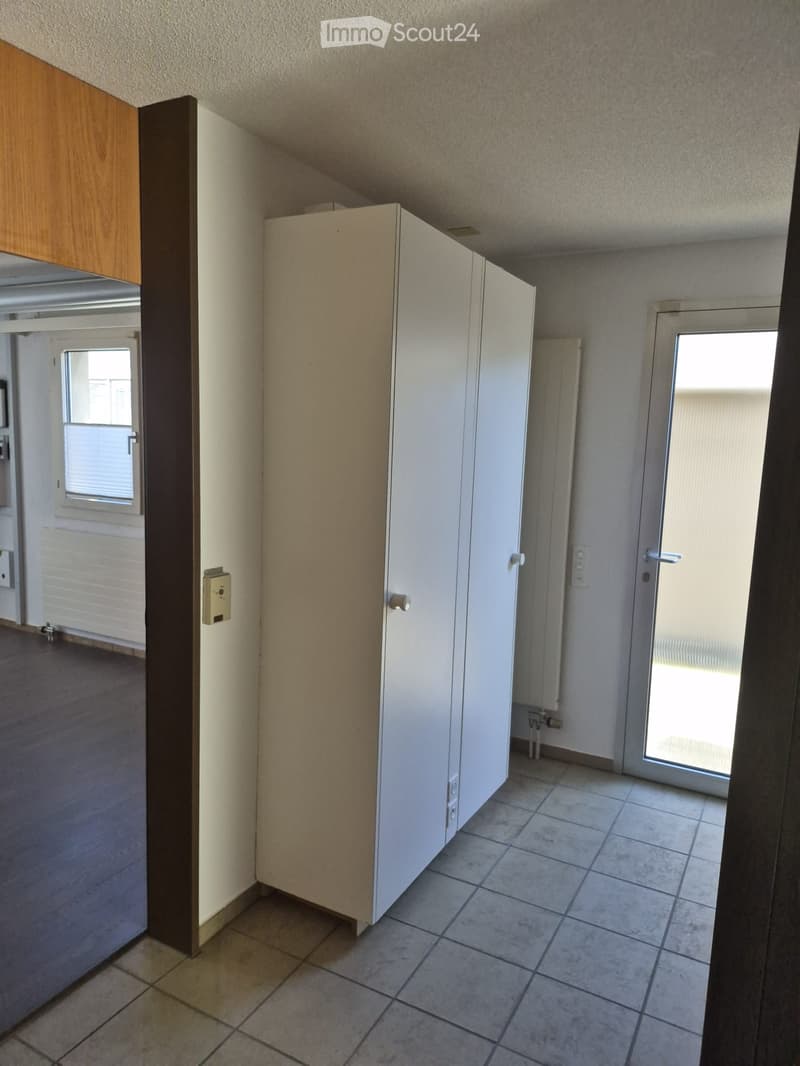 Empty room with tiled floor, white walls, and a sliding glass door leading outside. There is a white cabinet and a wooden door visible.
