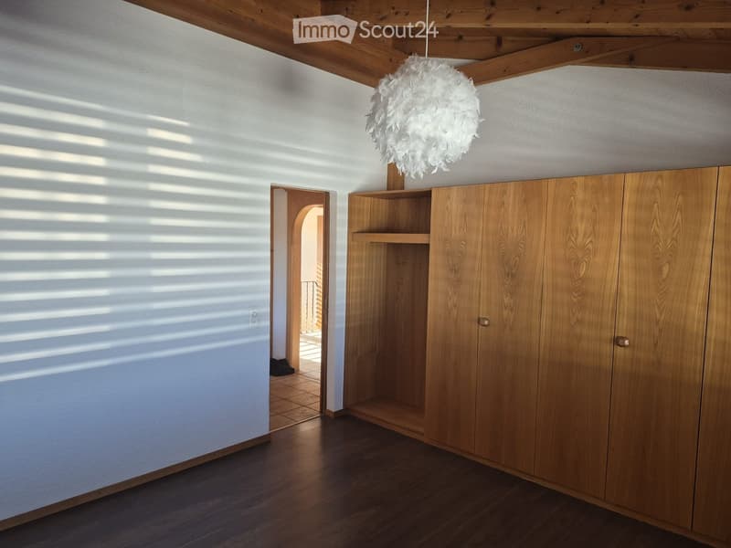 Empty hallway with wooden floor, white walls, built-in wooden cabinet with shelves, and a hanging decorative light fixture.