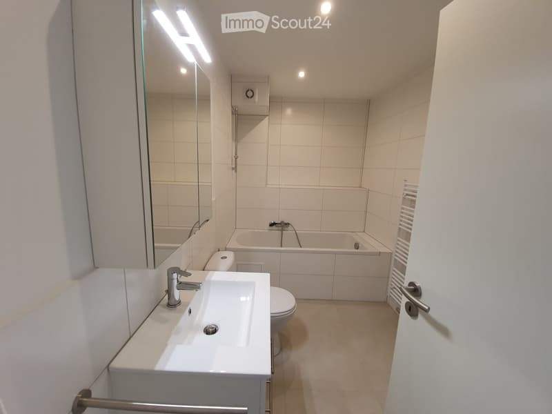 modern bathroom with white tiles, bathtub, toilet, sink, mirror, and towel rack