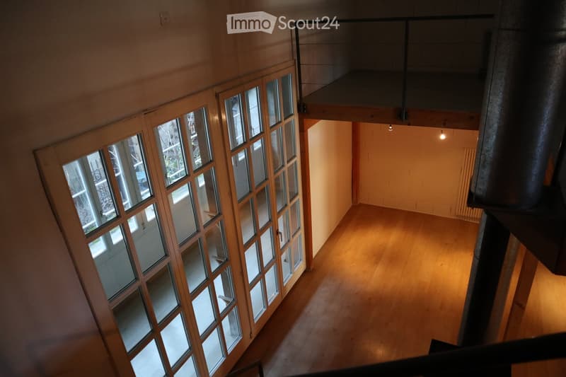 Empty room with wooden flooring, large windows, and a visible staircase leading to an upper level.