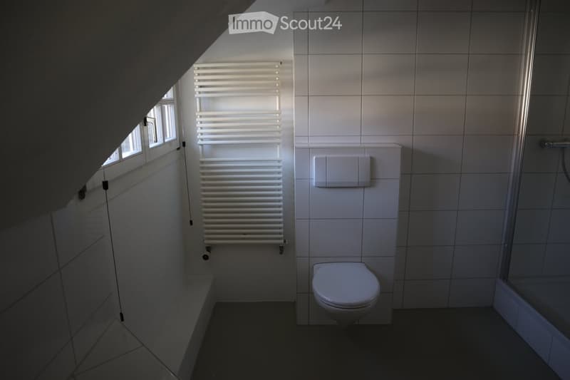Modern bathroom with white tiled walls, a toilet, a radiator, and a bathtub, featuring a window for natural light.