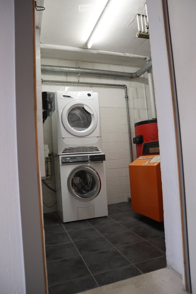 Utility room with a stacked washing machine and dryer, tiled walls, and dark tiled floor.