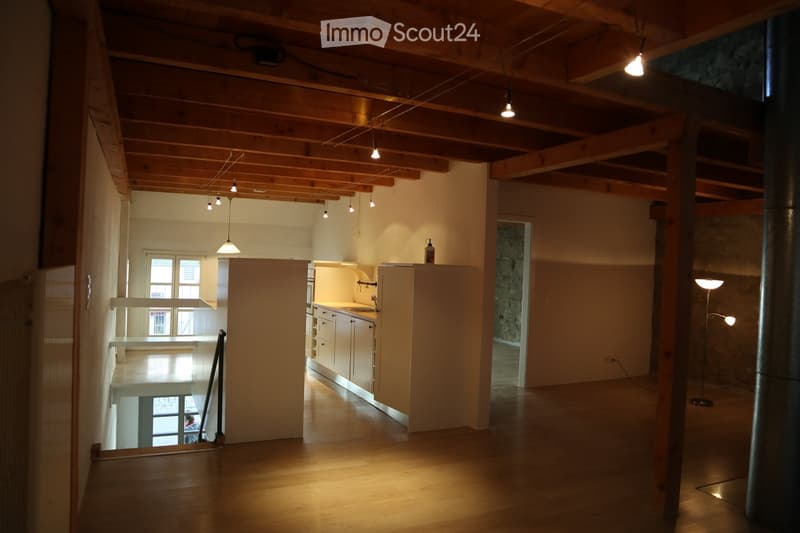 Open-plan living space with exposed wooden beams, a small kitchen area with cabinets and a sink, and a tall floor lamp in the corner.