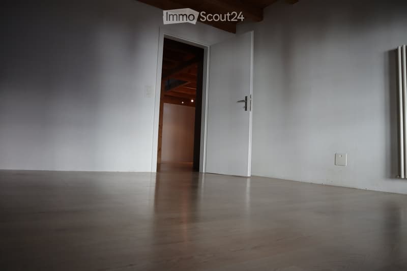 Empty room with wooden flooring, white walls, and a partially open door leading to another room.