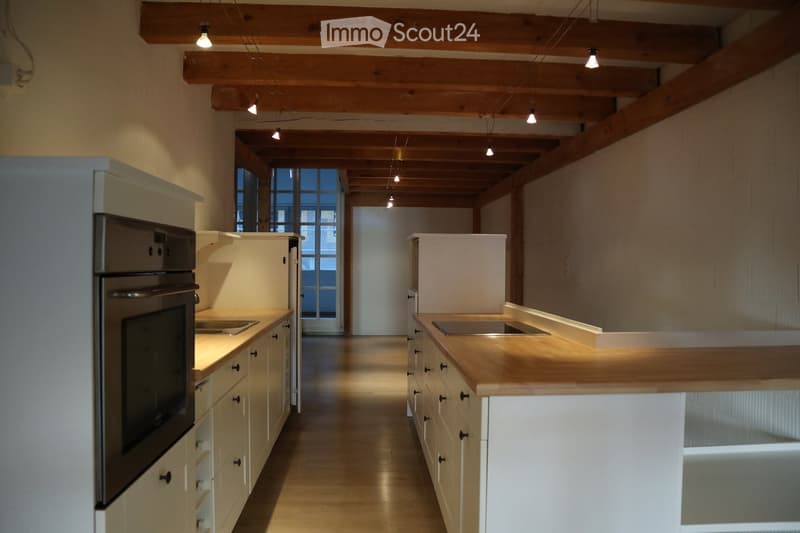 Modern kitchen with white cabinets, wooden countertops, stainless steel appliances, and exposed wooden beams on the ceiling.