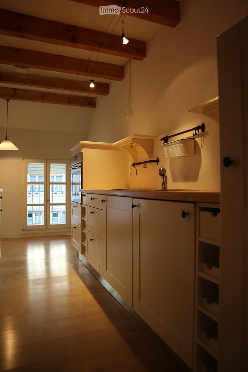 Bright kitchen with wooden cabinets, a sink, and an oven, illuminated by warm lighting and natural light from a large window.