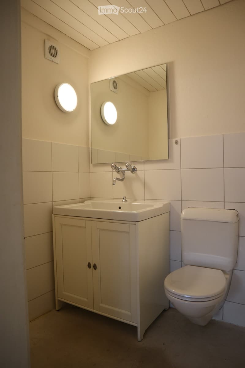 Modern bathroom with a white sink, toilet, and mirrored cabinet. Features round wall lights and tiled walls.
