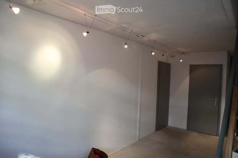 Empty room with white walls, grey doors, and track lighting. No furniture or equipment present.
