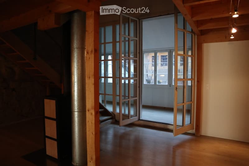 Empty room with wooden flooring, large glass doors leading to a balcony, and exposed wooden beams on the ceiling.