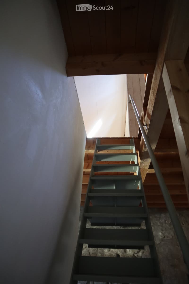 A modern staircase with wooden steps and a metal railing, leading upwards with natural light coming from the top.