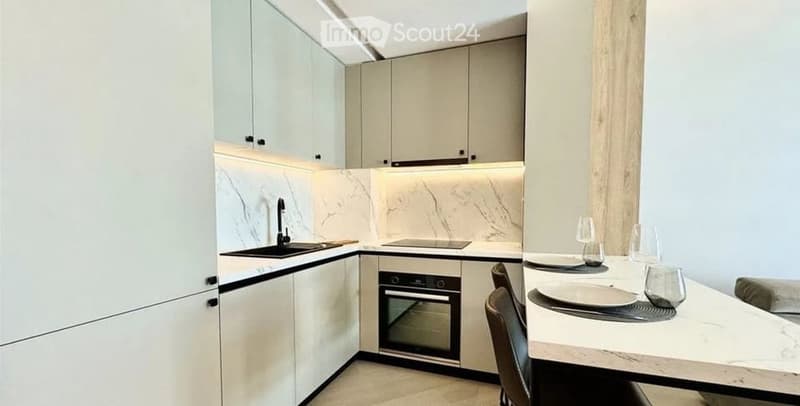 Modern kitchen with white cabinets, marble backsplash, built-in oven, sink, and a small dining area with a table and chairs.