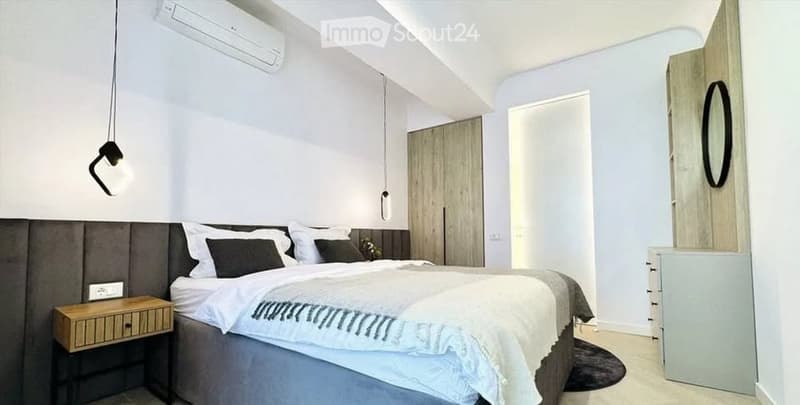 Modern bedroom with a large bed, nightstand, wardrobe, and air conditioner. Features pendant lights and a sleek design.