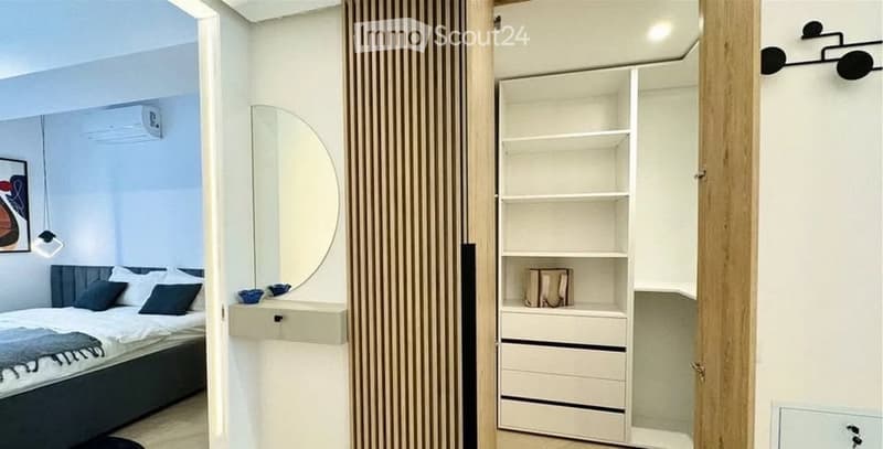 Modern bedroom with a large bed, nightstand, round mirror, and built-in wardrobe with shelves and drawers.