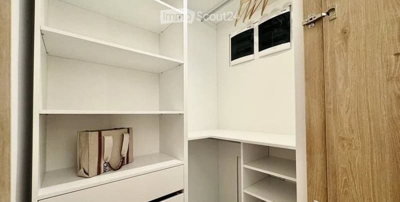 A neatly organized closet with white shelves and a wooden door, featuring a single handbag placed on one of the shelves.