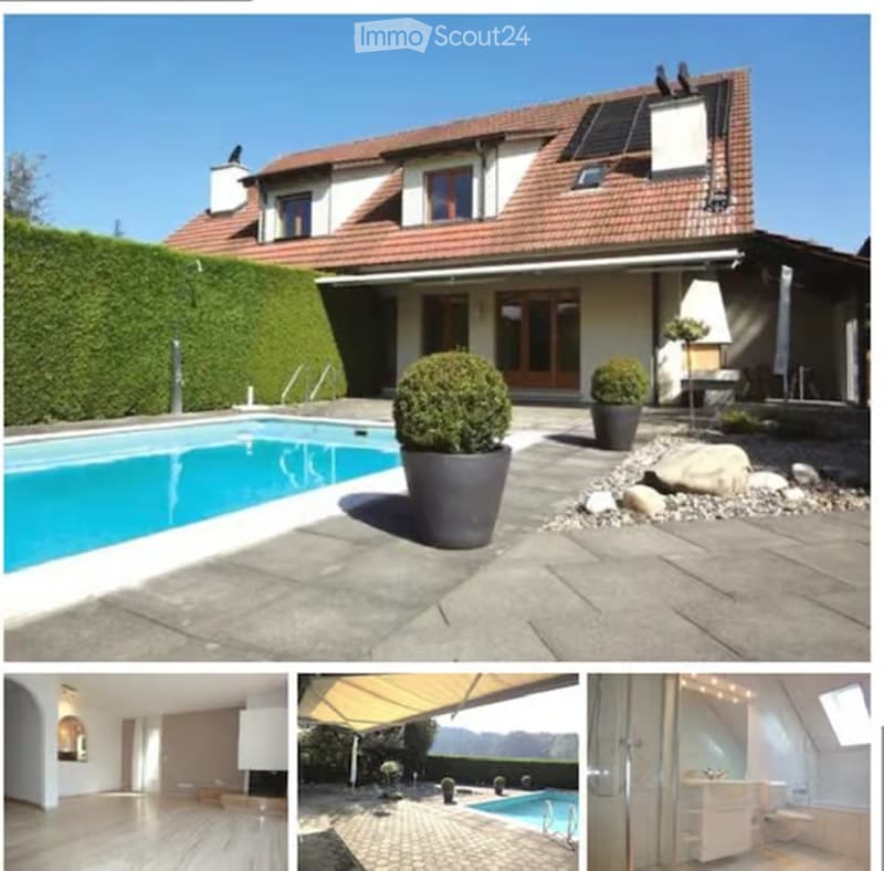 Two-story house with red-tiled roof, large windows, and solar panels on the roof. The property features a swimming pool in the garden area, surrounded by potted plants and a neatly trimmed hedge.
