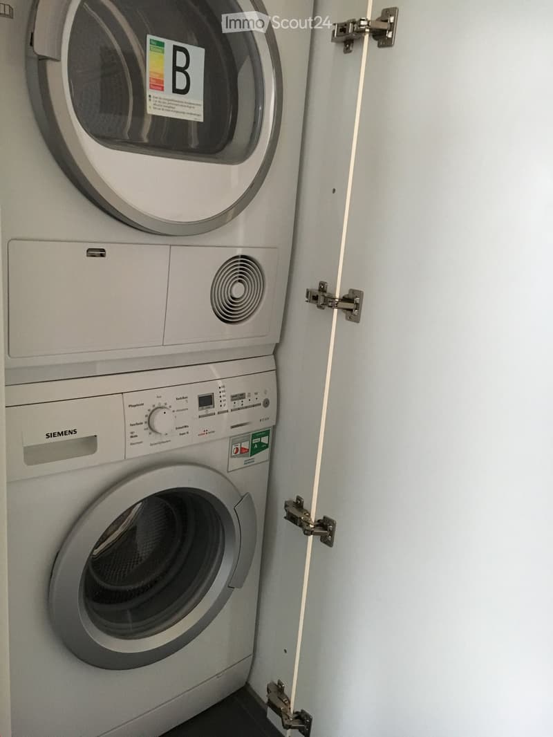 A compact bathroom with a stacked washing machine and dryer unit, featuring control panels and a door with hinges.
