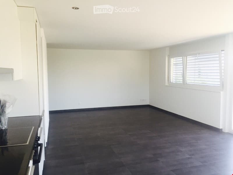 Empty room with white walls, dark wooden flooring, and a window with blinds. No furniture or equipment is present.