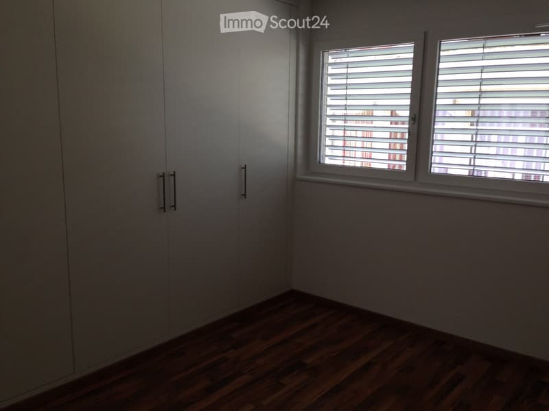 Empty room with wooden flooring, large built-in wardrobe, and two windows with blinds.