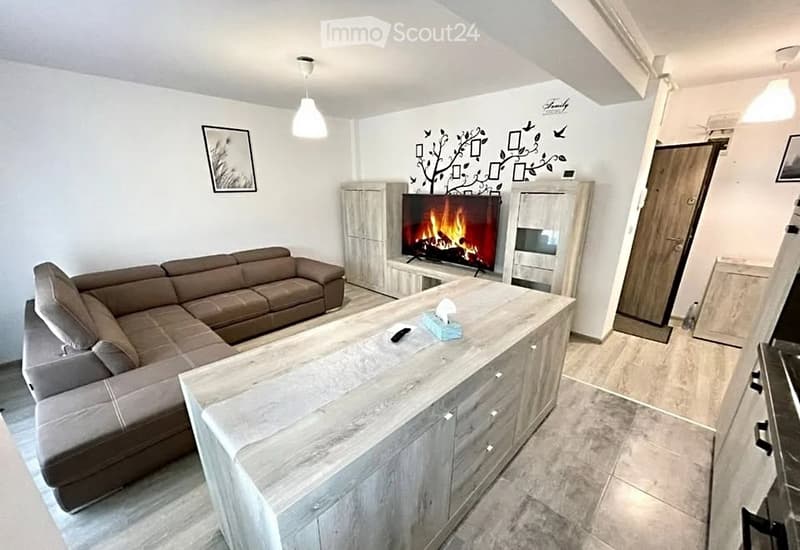 Modern living room with a grey sectional sofa, a large coffee table, a TV with a fireplace effect, and a decorative wall design.