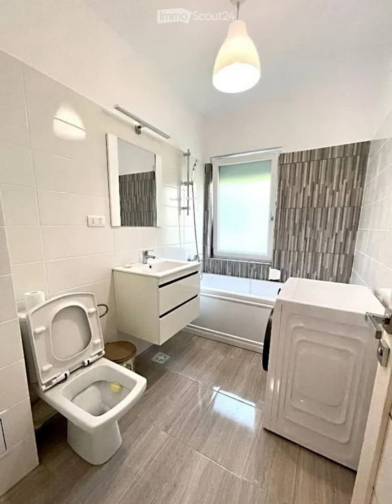 Modern bathroom with white tiles, a toilet, a sink with a cabinet, a bathtub, a mirror, and a hanging light fixture.