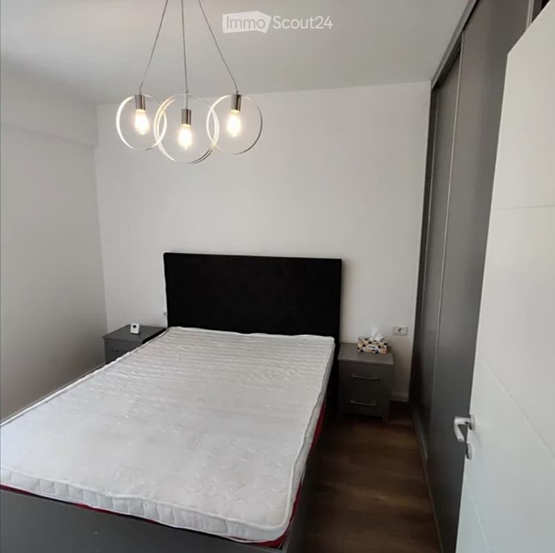 Modern bedroom with a white mattress on a dark headboard, two nightstands, and a hanging pendant light fixture with clear glass shades.