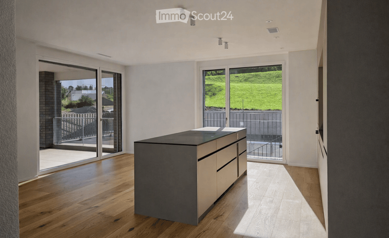 Modern kitchen with a central island, wooden flooring, and large glass sliding doors leading to an outdoor area.