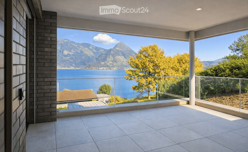 Modern balcony with large glass railings, tiled floor, and panoramic view of a lake and mountains.