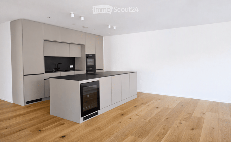 Modern kitchen with light grey cabinets, a central island with a black countertop, and built-in appliances including an oven and sink.