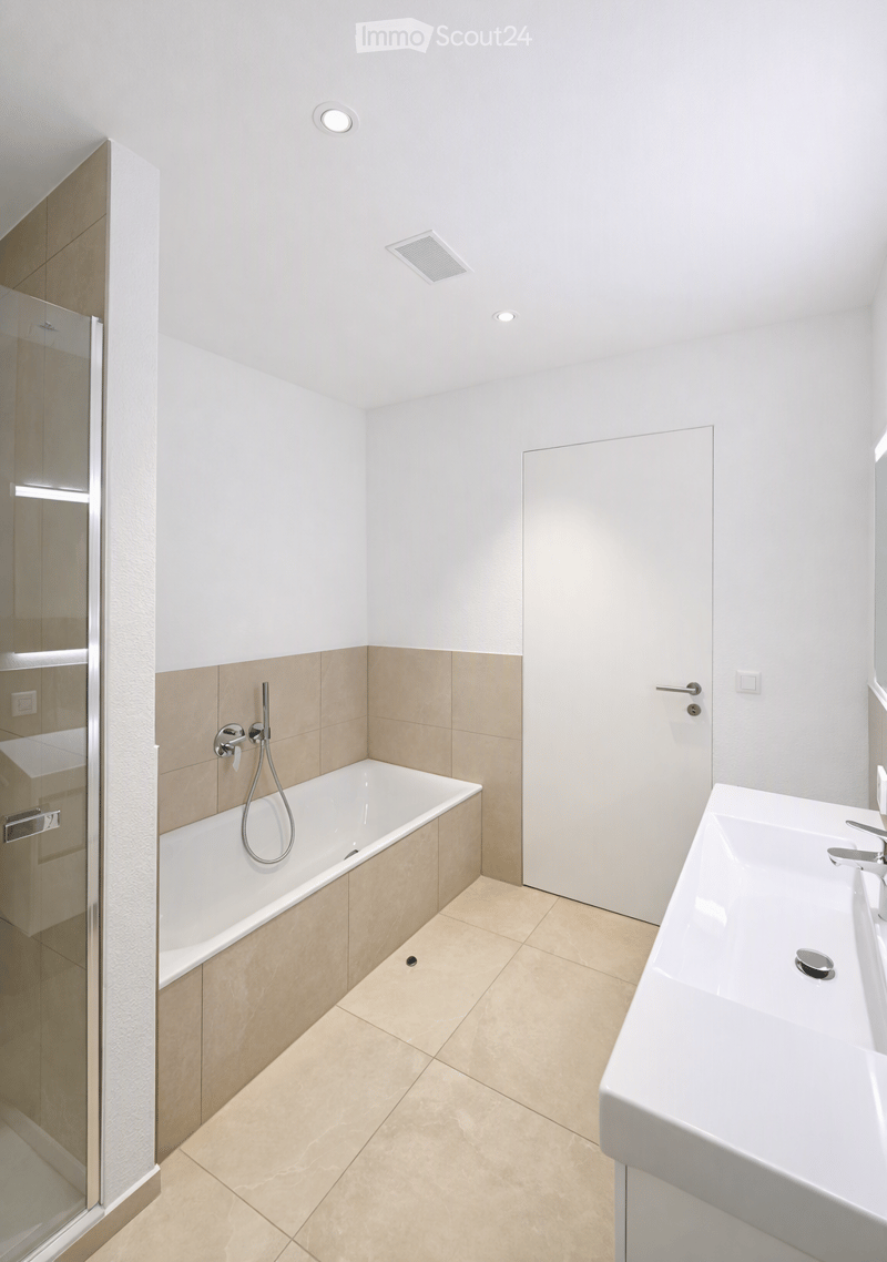 Modern bathroom with a white bathtub, a double sink, a glass shower enclosure, and beige tiles.