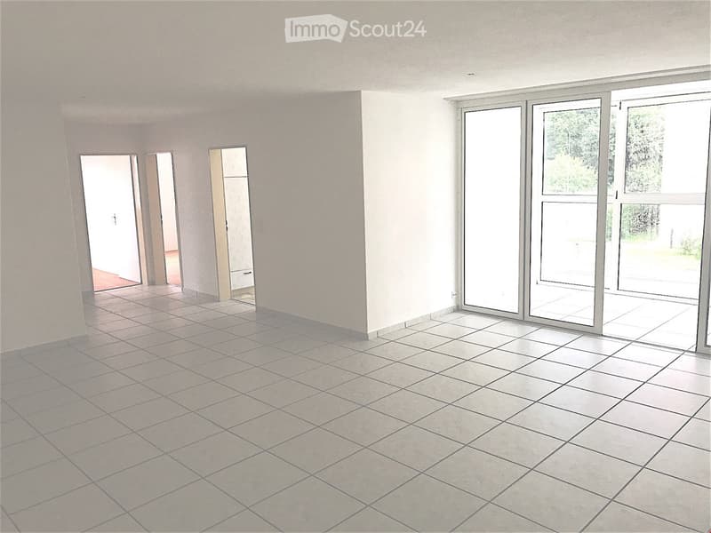 Empty room with white tiles, sliding glass doors, and a view of trees outside