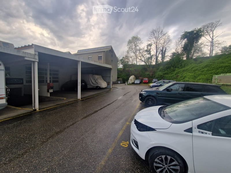 A multi-level parking garage with several cars parked inside and outside, surrounded by trees and a grassy hill.