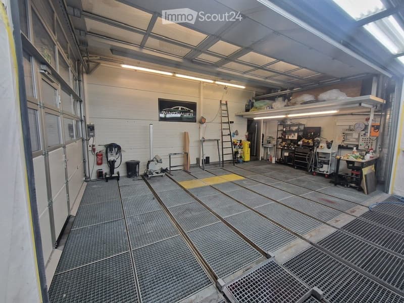A spacious garage with metal flooring, large windows, and various tools and equipment including a ladder, workbench, and tool cabinets.