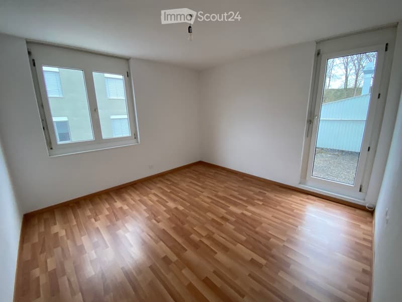 Empty room with wooden flooring, white walls, and large windows with blinds. No furniture or equipment present.