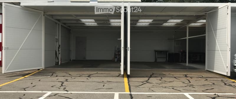 Large, open garage with multiple parking spaces, white walls, and a concrete floor. The garage doors are open, revealing a clean and organized space.