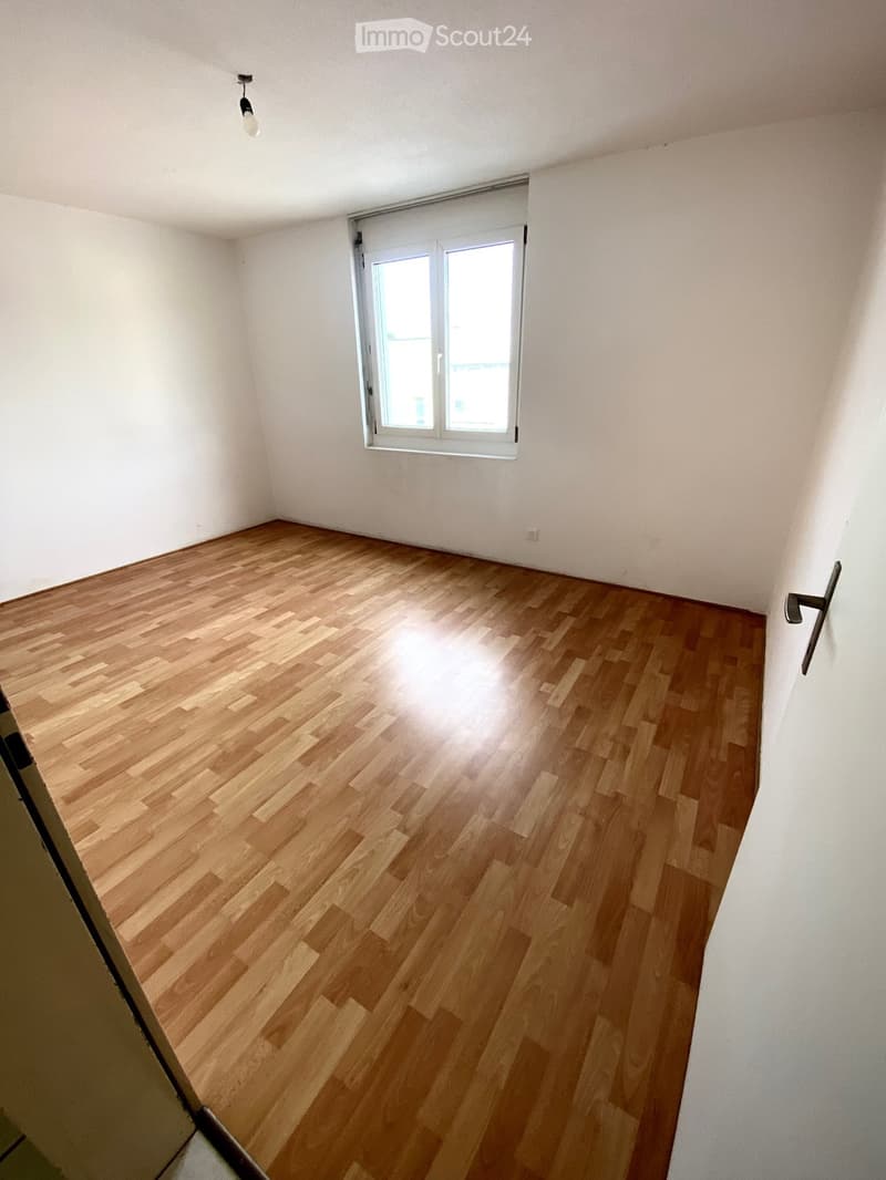 Spacious bedroom with hardwood flooring, white walls, and a single window providing natural light.