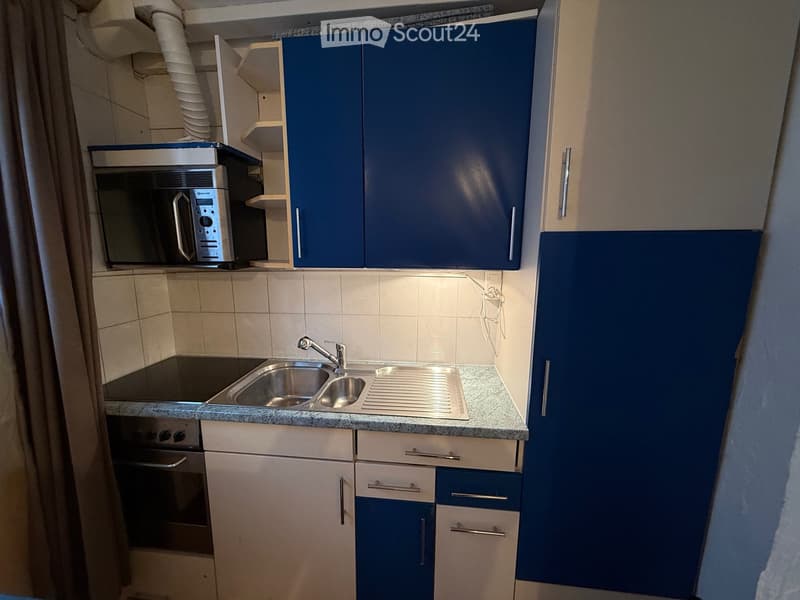 Stainless steel sink, electric stove, blue and white cabinets, microwave, tiled walls