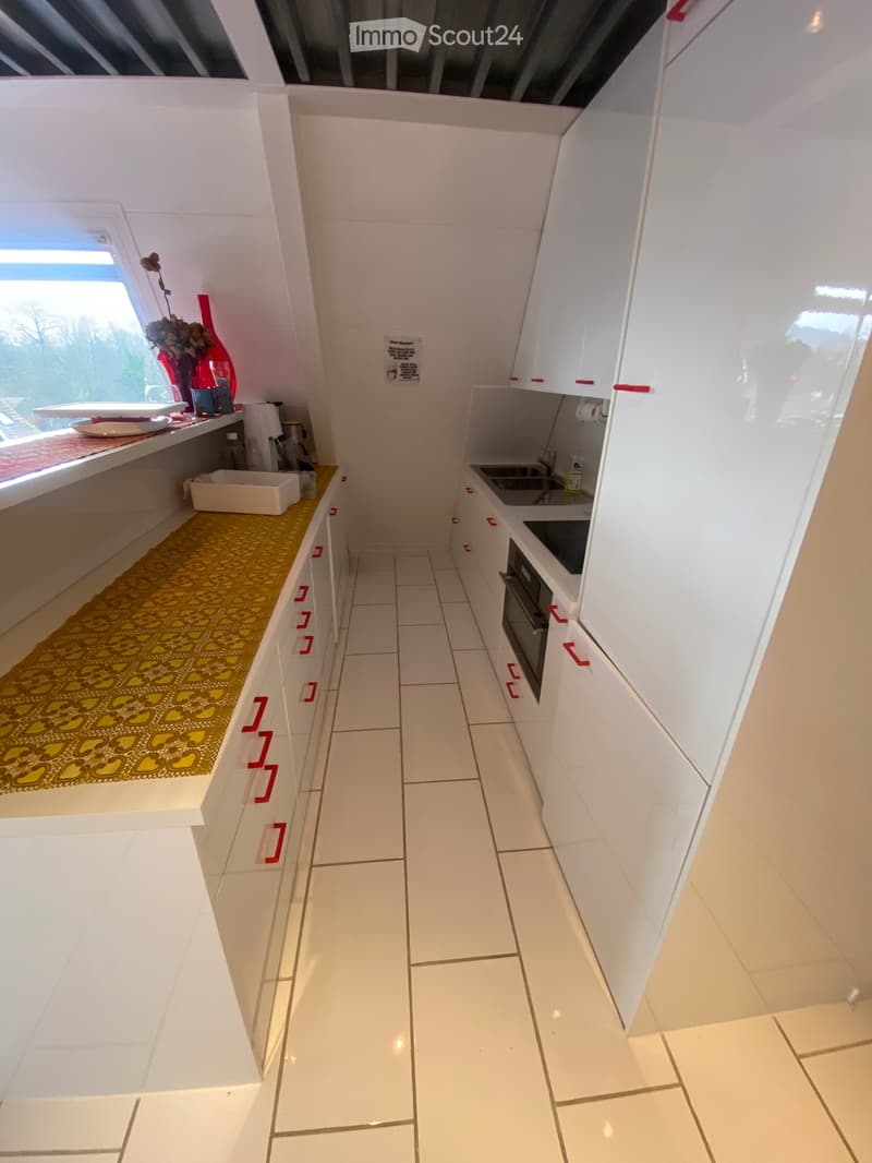 Modern kitchen with white cabinets, tiled floor, and a window. Includes a sink, oven, and various small appliances.