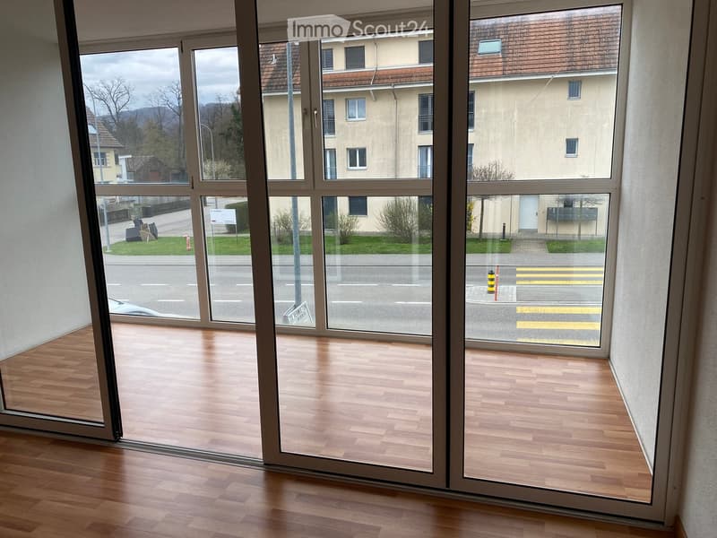 Empty room with wooden flooring and large glass sliding doors leading to a street view.