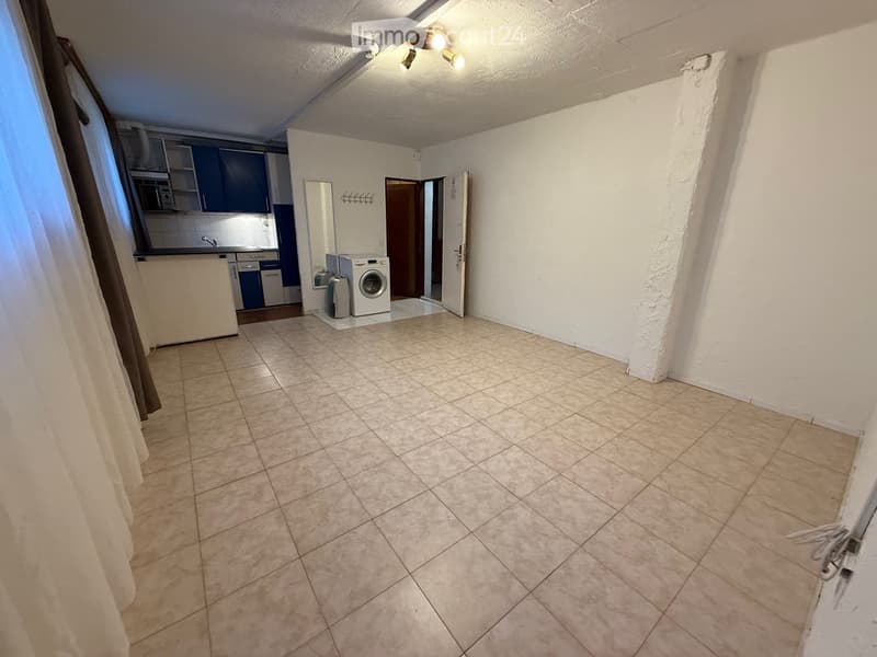 Empty room, white walls, tiled floor, white ceiling with lights, washing machine, entrance to the kitchen