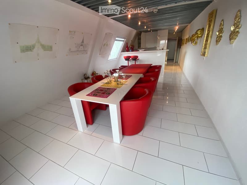 Modern dining area with white tiled flooring, white table, red chairs, and decorative items on the walls.