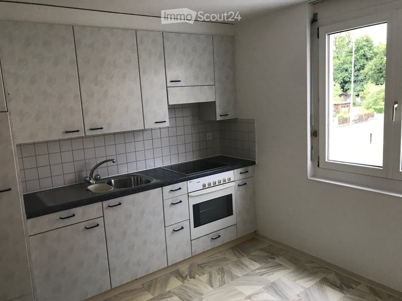Modern kitchen with gray cabinets, black countertop, built-in oven and stove, sink, and tiled backsplash. Large window providing natural light.