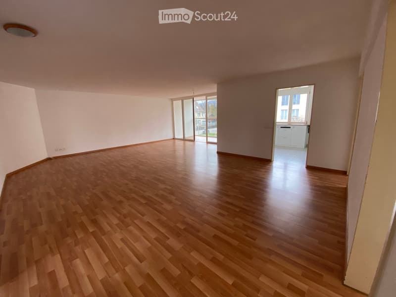 Empty room with wooden flooring, white walls, and large windows with sliding glass doors leading to an outdoor area.